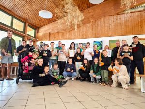 Visi stovyklos dalyviai ir vaikai susirinkę salėje bendrai nuotraukai laiko rankose savo pagamintus molio dirbinius.